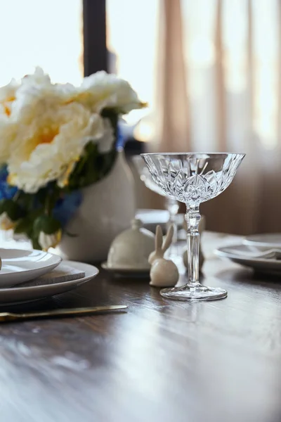 Selective focus of crystal glass, bouquet in vase and decorative bunnie on wooden table at home — Stock Photo