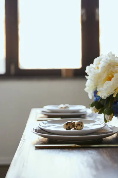 Fuoco selettivo di uova di quaglia su piatti bianchi vicino a fiori su tavolo di legno a casa — Foto stock