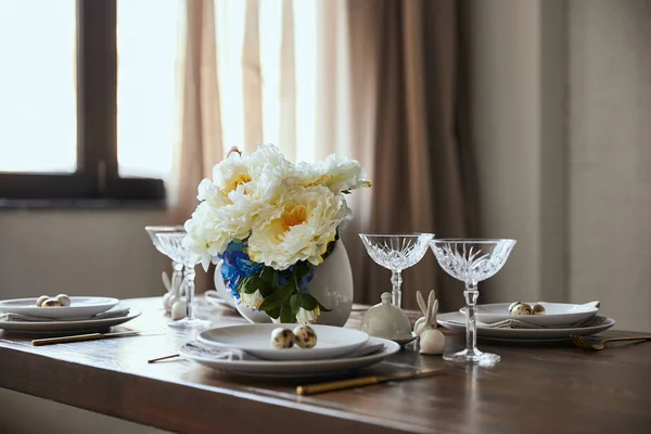 Oeufs de caille sur des assiettes blanches, fleurs dans un vase et verres en cristal sur une table en bois à la maison — Photo de stock