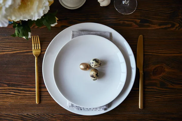 Top view of quail eggs on white plates near fork and knife on wooden table — Stock Photo