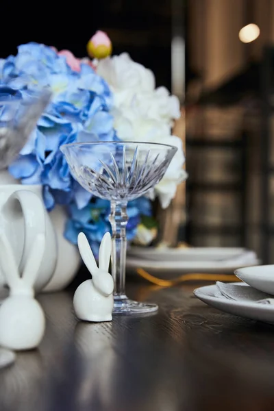 Focus selettivo di conigli decorativi vicino a vetro cristallo e fiori sul tavolo in legno a casa — Foto stock