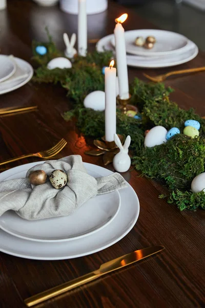 Foco selectivo de huevos de codorniz en servilletas y platos cerca de musgo verde y velas ardientes en mesa de madera - foto de stock