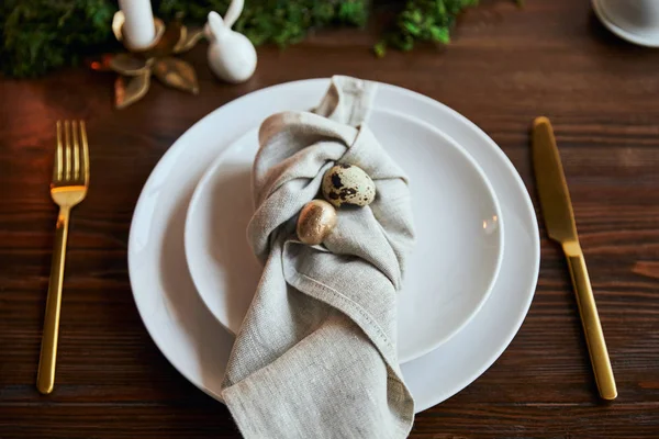 Selective focus of quail eggs on napkin and plates near green moss and cutlery on wooden table — Stock Photo