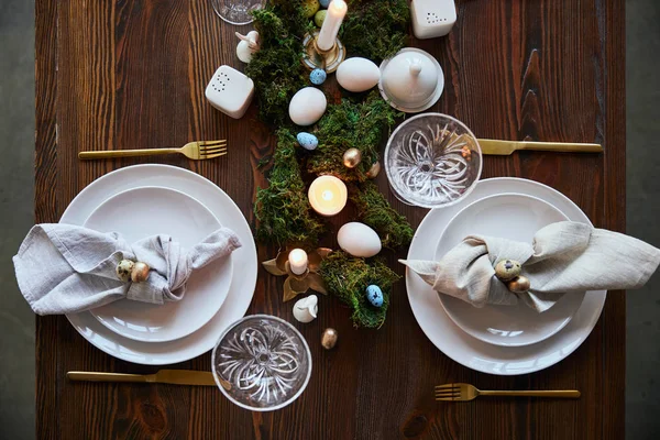 Top view of quail eggs on napkin and plates near green moss, candles and crystal glasses on wooden table — Stock Photo