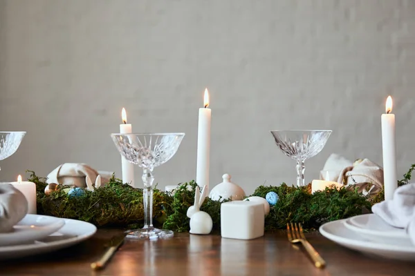 Verres en cristal, bougies allumées, mousse verte et oeufs de caille sur la serviette et la vaisselle à la maison — Photo de stock