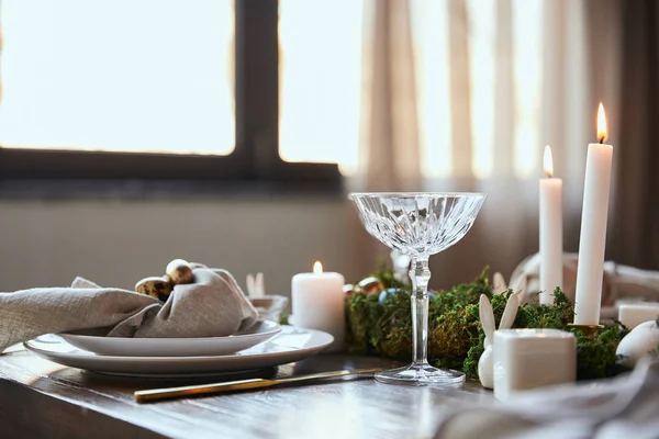 Selective focus of quail eggs on napkin and plates near green moss, burning candles and crystal glass on wooden table at home — Stock Photo