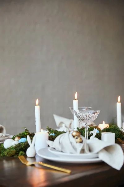 Selective focus of quail eggs on napkin and plates near green moss, candles and crystal glasses on wooden table at home — Stock Photo