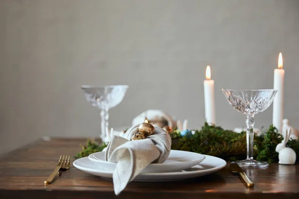 Foyer sélectif des oeufs de caille sur la serviette et les assiettes, mousse verte, bougies et verres en cristal sur la table en bois à la maison — Photo de stock