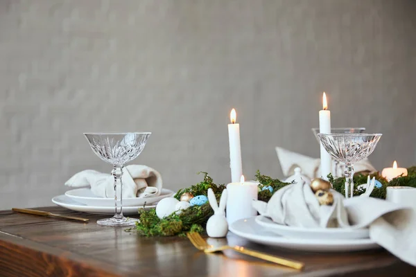 Foco seletivo de ovos de codorna em guardanapo e placas, musgo verde, velas, óculos de cristal e coelho decorativo na mesa de madeira em casa — Fotografia de Stock