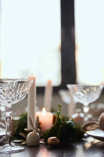Fuoco selettivo di coniglio decorativo vicino a candela e bicchieri di cristallo sul tavolo di legno a casa — Foto stock