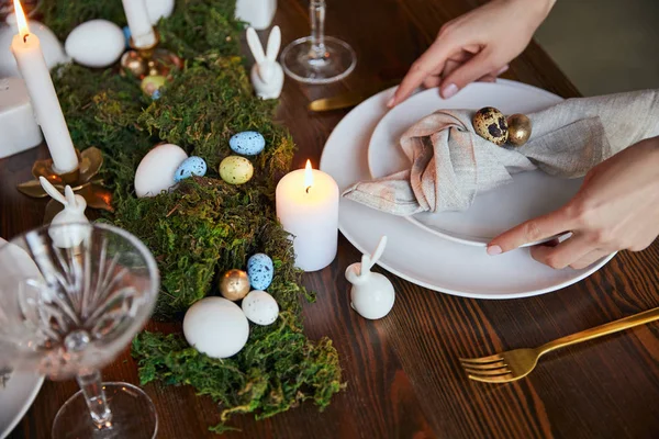 Vue recadrée de la femme mettant des assiettes près des bougies brûlantes et de la mousse sur une table en bois à la maison — Photo de stock