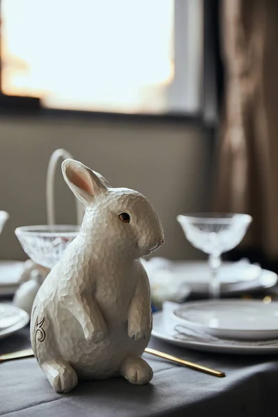 Selektiver Fokus des dekorativen Hasen in der Nähe von Tellern und Kristallgläsern auf dem heimischen Tisch — Stockfoto