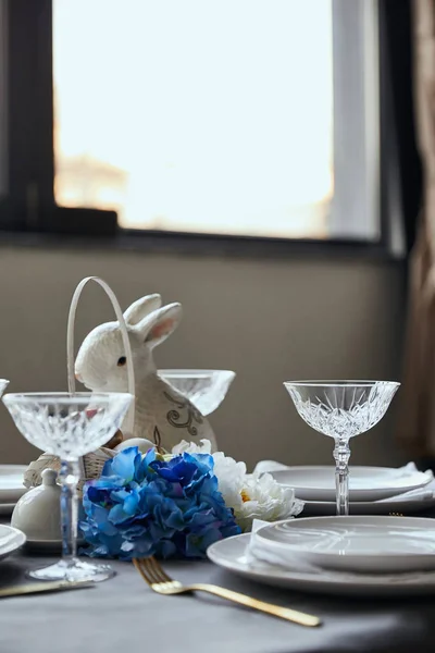 Plates, crystal glass, decorative bunnie and flowers on table at home — Stock Photo