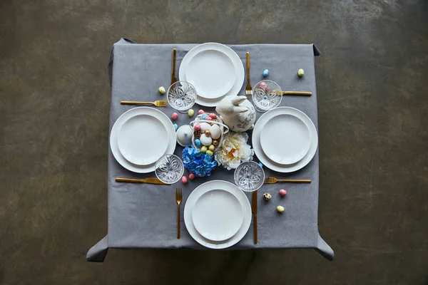 Top view of table with white plates, cutlery, crystal glasses, cutlery, painted eggs and flowers at home — Stock Photo