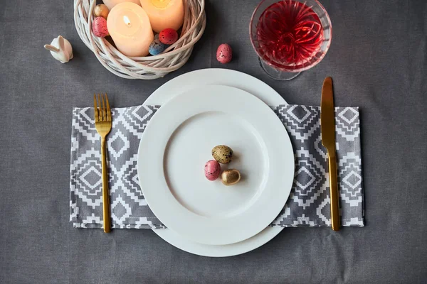 Top view of plates with cloth napkin, eggs and burning candles in basket, wine in crystal glass on table at home — Stock Photo