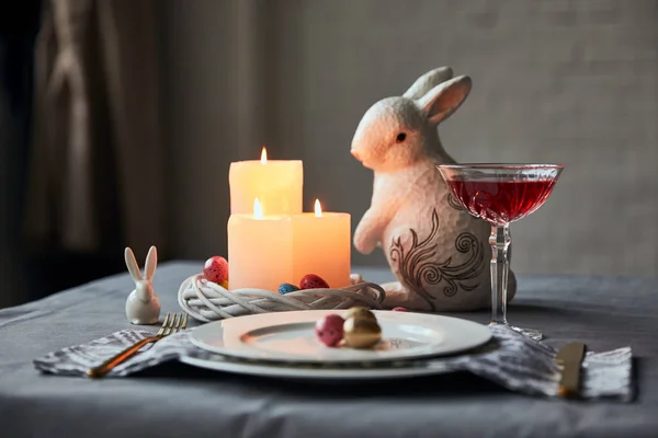 Foyer sélectif des assiettes avec des œufs, du vin en verre de cristal, des bougies allumées et des lapins décoratifs sur la table à la maison — Photo de stock