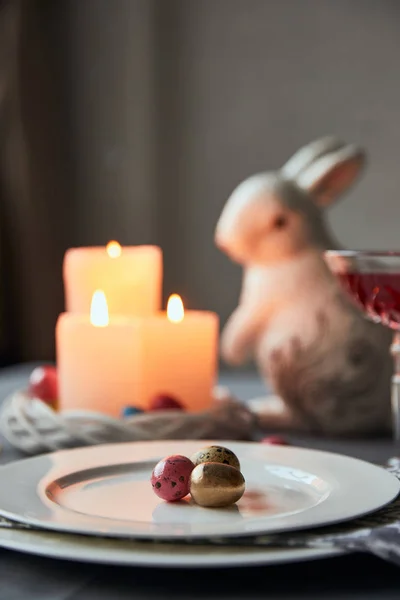 Messa a fuoco selettiva di piatti con uova colorate, vino in cristallo, candele e coniglietti decorativi in tavola a casa — Foto stock