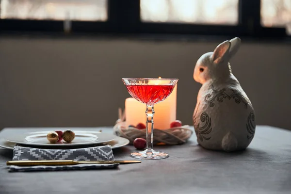 Focus selettivo di coniglietti decorativi, piatti con uova, vino in cristallo, candele in tavola a casa — Foto stock