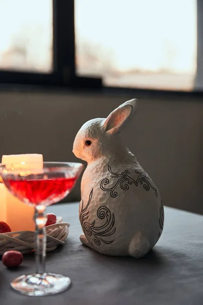 Conejito decorativo, huevos, vino en cristal y velas encendidas en la mesa en casa - foto de stock