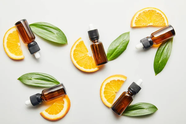 Flat lay with orange slices and bottles with essential oil on grey background — Stock Photo