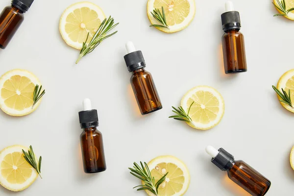 Flat lay with essential oil in bottles, lemon slices and rosemary on grey background — Stock Photo