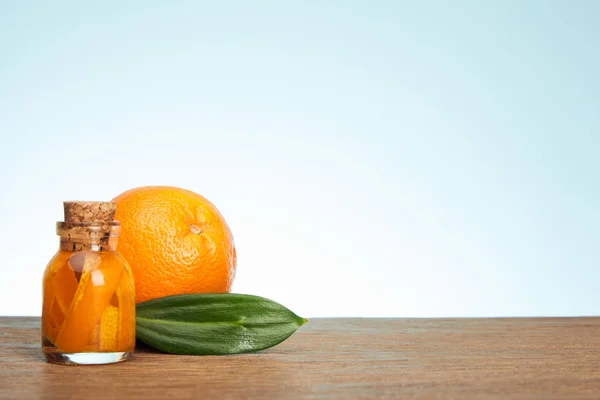 Glass bottle and ripe orange with green leaf on wooden surface — Stock Photo