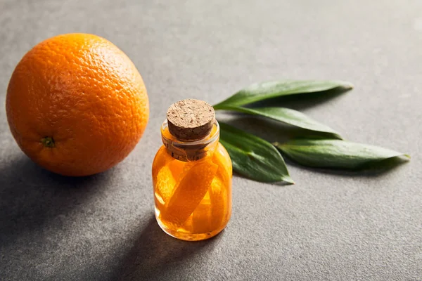 Ganze reife Orange und Flasche mit ätherischem Öl auf dunkler Oberfläche — Stockfoto
