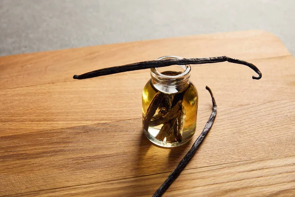 Vanilla pods with glass bottle of essential oil on wooden cutting board — Stock Photo