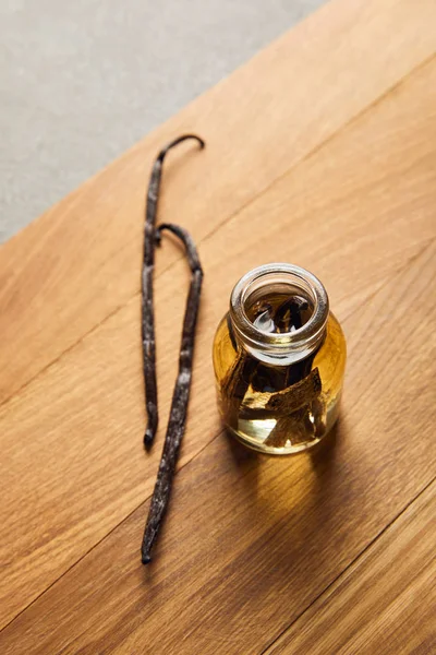 Top view of essential oil with vanilla pods on wooden surface — Stock Photo