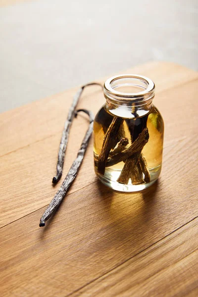 Стеклянная бутылка эфирного масла с ванильными стручками на деревянной доске — стоковое фото