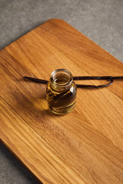 Стеклянная бутылка эфирного масла с ванильными стручками на деревянной доске — стоковое фото