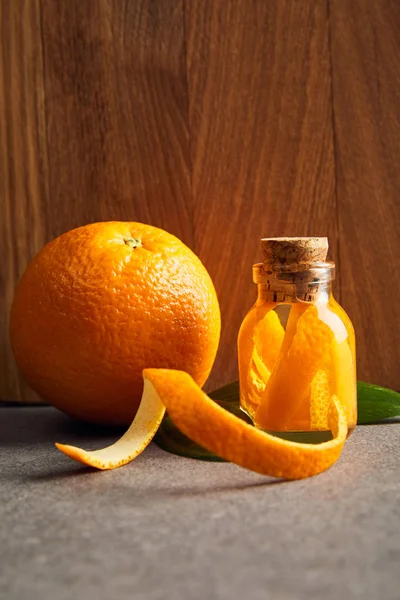 Aceite esencial y naranja maduro en botella de vidrio sobre fondo de madera - foto de stock