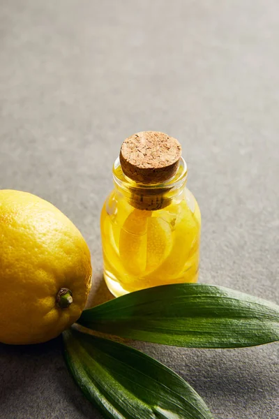Limão maduro com folhas verdes e garrafa de vidro com óleo essencial na superfície escura — Fotografia de Stock
