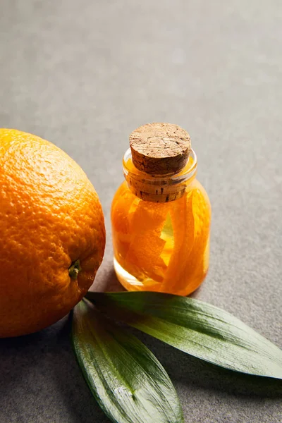 Спелый апельсин со стеклянной бутылкой эфирного масла на темной поверхности — стоковое фото