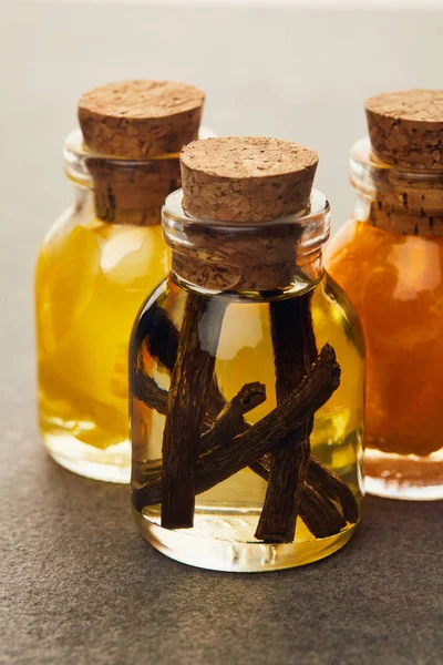 Frascos de vidrio de aceite esencial con vainilla y frutas cortadas en superficie oscura - foto de stock