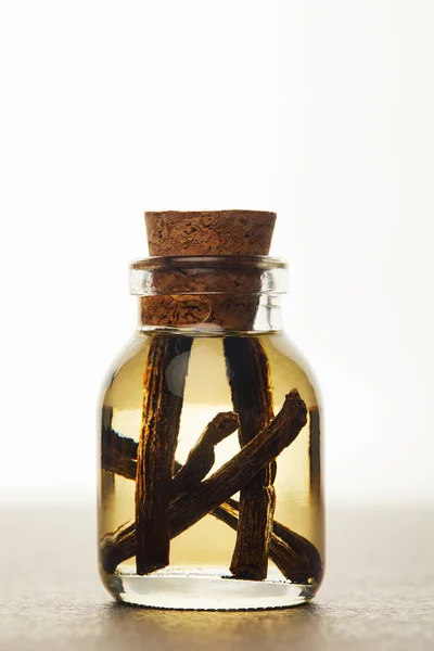 Glass bottle of essential oil with vanilla pods on white background — Stock Photo