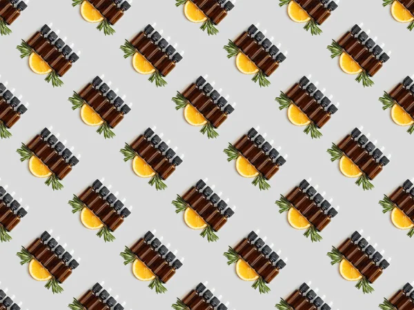 Padrão com garrafas de óleo essencial e fatias de laranja no fundo cinza — Fotografia de Stock