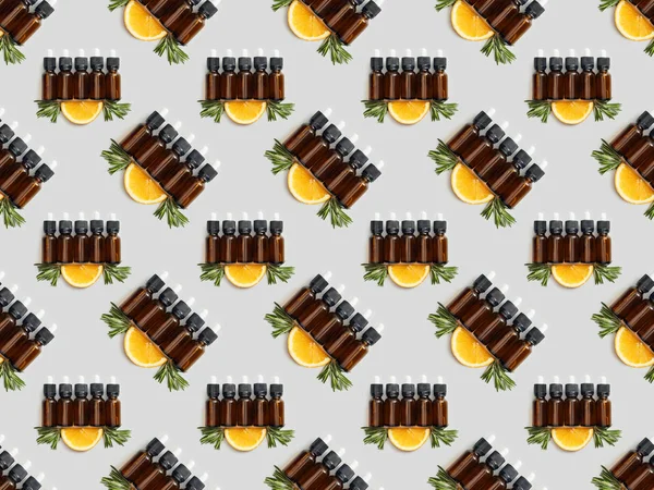 Patrón con botellas marrones con aceite esencial y naranja en rodajas sobre fondo gris - foto de stock