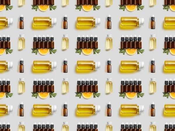 Pattern with various bottles of essential oil and cut orange on grey background — Stock Photo