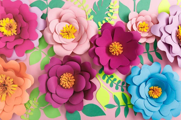 Vue du dessus des fleurs colorées en papier et des plantes vertes sur fond rose — Photo de stock