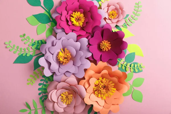 Vista superior de flores de papel, hojas verdes y amarillas sobre fondo rosa - foto de stock