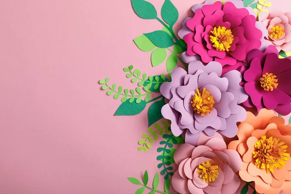 Top view of colorful paper flowers and green leaves on pink background — Stock Photo