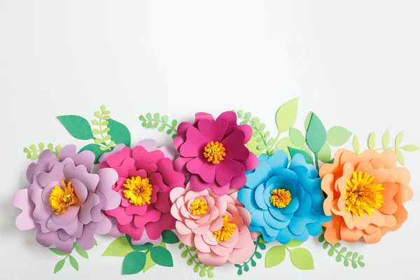 Draufsicht auf bunte Papierblumen und grüne Blätter auf grauem Hintergrund — Stockfoto