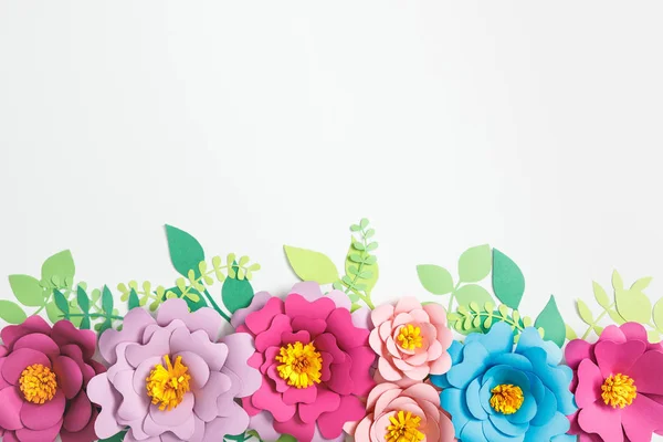 Draufsicht auf bunte Papierblumen und grüne Blätter auf grauem Hintergrund — Stockfoto