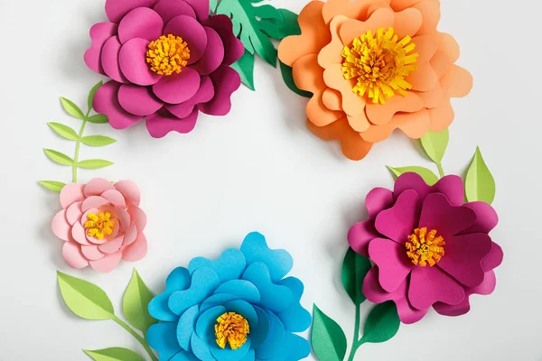 Top view of multicolored paper flowers and green leaves on grey background — Stock Photo