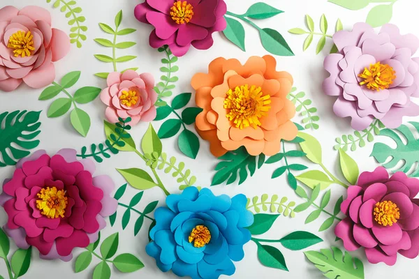 Top view of colorful paper flowers and green leaves on grey background — Stock Photo