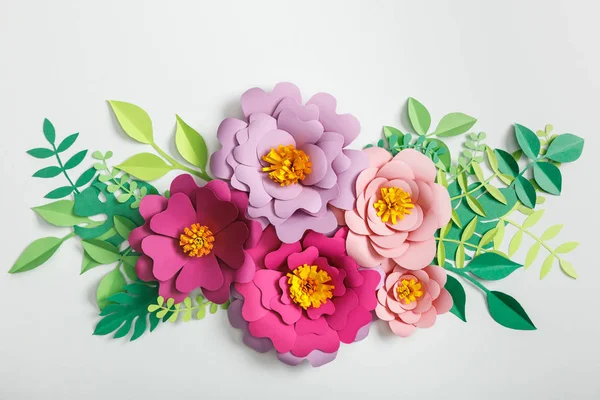 Top view of pink and lilac paper flowers with green leaves on grey background — Stock Photo