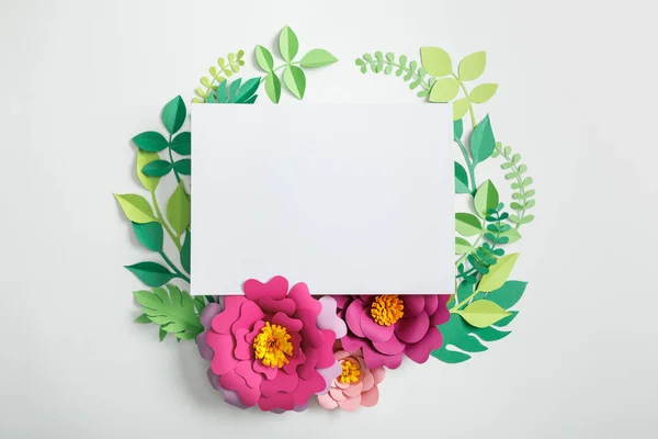 Top view of white blank card near pink paper flowers with green leaves on grey background — Stock Photo