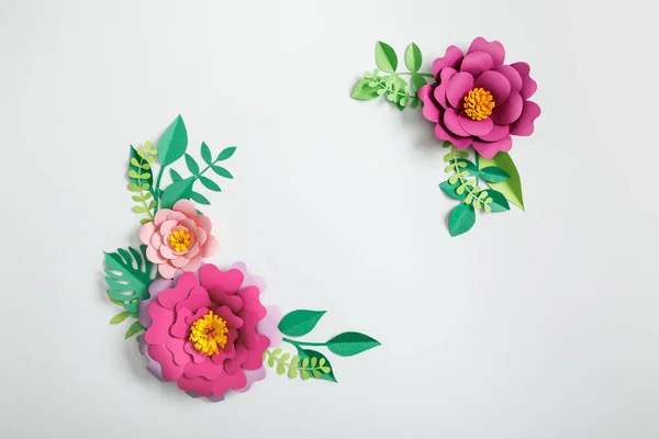 Top view of paper flowers and green plants with leaves on grey background — Stock Photo