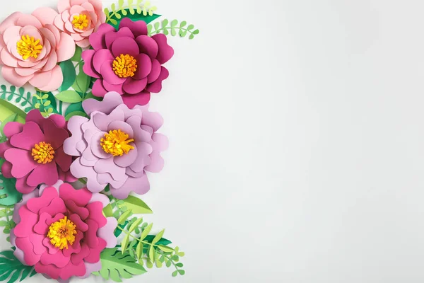 Draufsicht auf rosa und lila Papierblumen und grüne Pflanzen mit Blättern auf grauem Hintergrund — Stockfoto